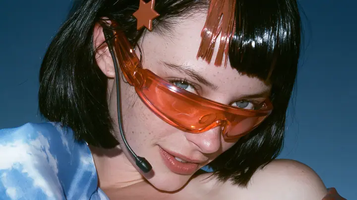 Y2K high fashion editorial, a 2001 couture magazine story: close-up of a Caucasian American woman in her mid-twenties with pale skin and light freckles, a glossy black blunt jaw-length bob with heavy straight bangs…