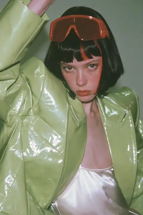Y2K high fashion editorial, a 2001 couture magazine story: full-length shot, head to toe with the feet in frame, of a young Caucasian American woman with pale skin and a glossy black blunt bob with heavy straight…